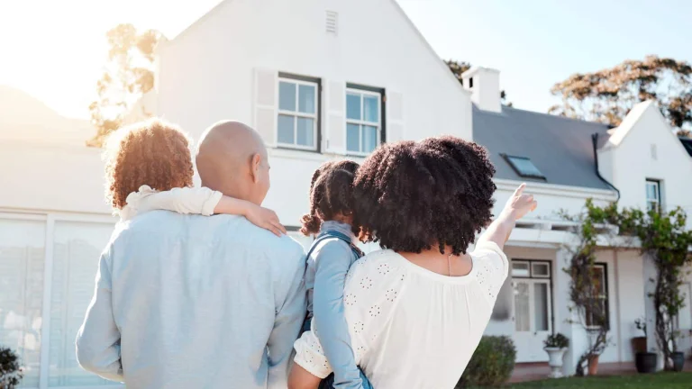 A family standing together outside their home looking at it on a sunny day