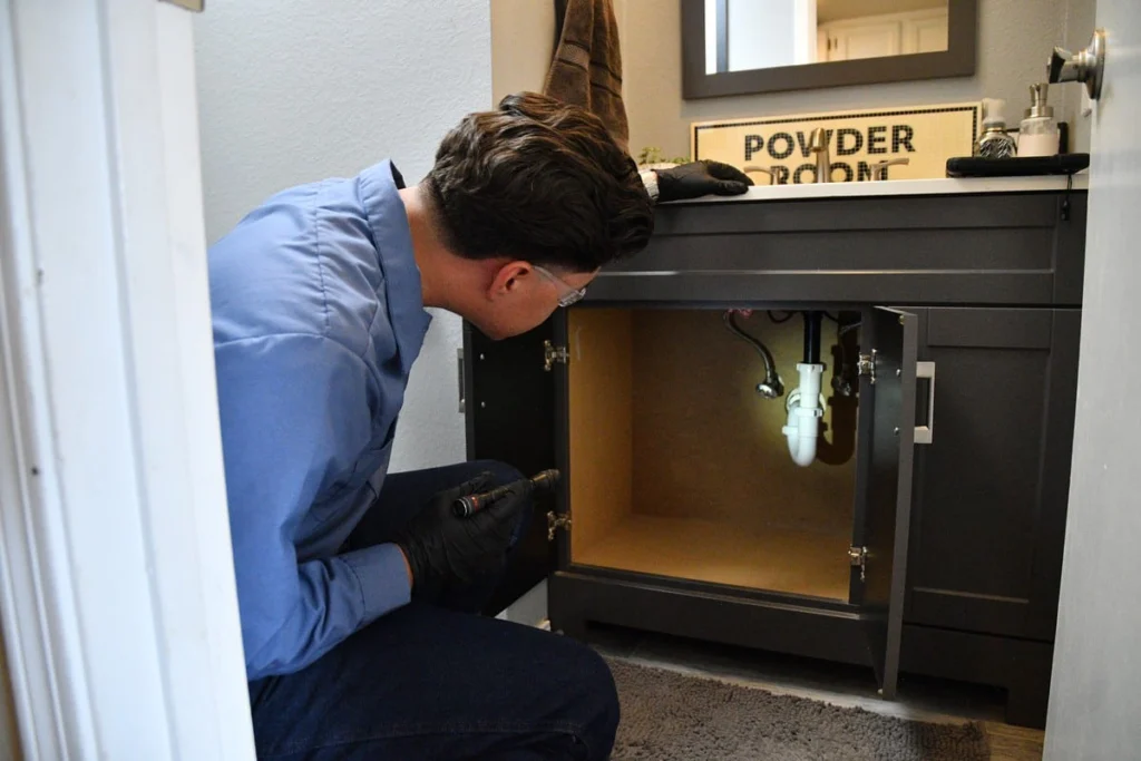 Plumber inspecting bathroom sink cabinet pipes in Albuquerque, NM