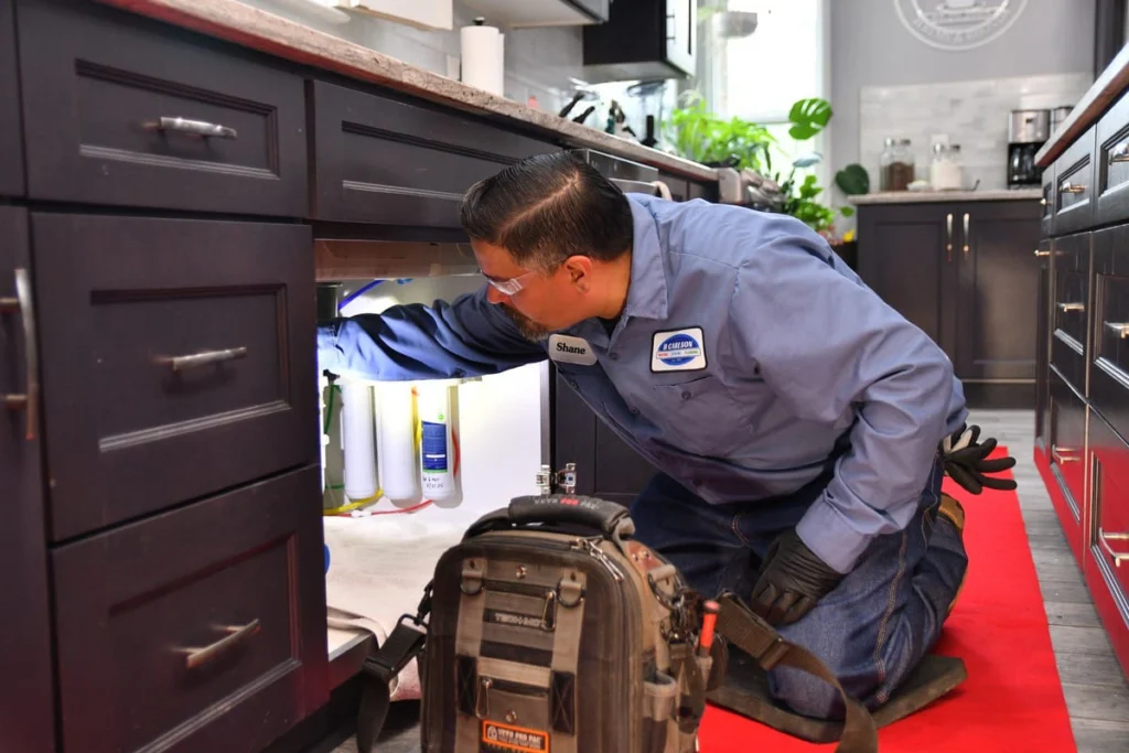 Professional plumber inspecting under cabinet in Albuquerque, NM