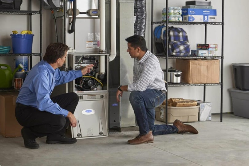 An HVAC technician explains the parts of a gas furnace to a home customer
