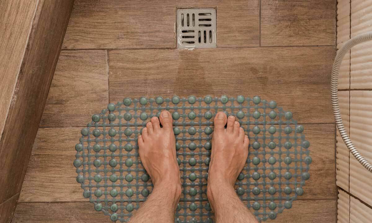 Someone standing barefoot on a mat near the shower floor drain