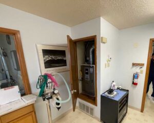 Equipment room in a veterinary clinic with furnace closet open and technician preparing for AC diagnostic.