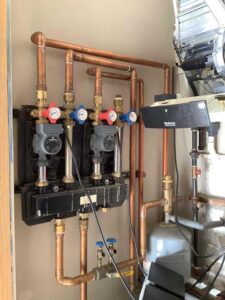 This photo shows the hydronic manifold with multiple circulator pumps and zone valves. These components control water flow to different heating zones in the home, ensuring balanced and efficient heat distribution.